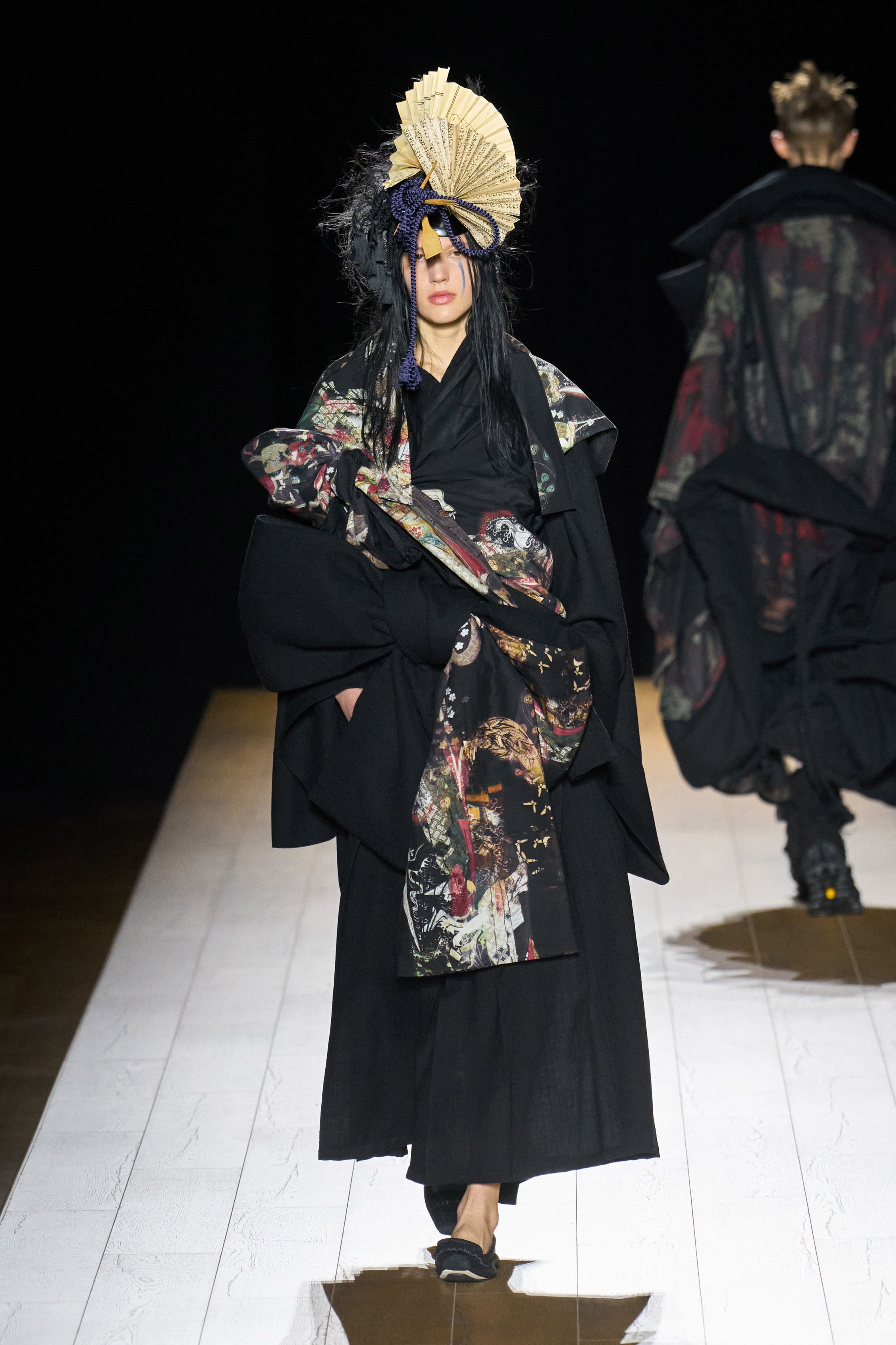 Yohji Yamamoto 本季依然延续标志性的黑色哲学：宽松层叠轮廓、和服式结构与手工拼接面料形成一种诗意而深沉的东方美学。夸张头饰与飘逸衣摆让整场秀像一场黑色戏剧，既神秘又极具艺术感-顽石频道趋势研究